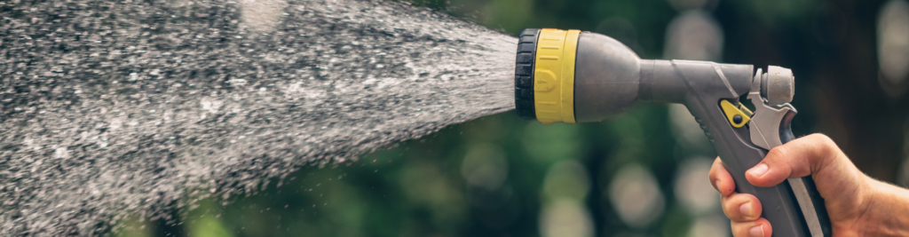 Eine Hand hält einen Wasserschlauch mit einer grau-gelben Düse aus der Wasser kommt
