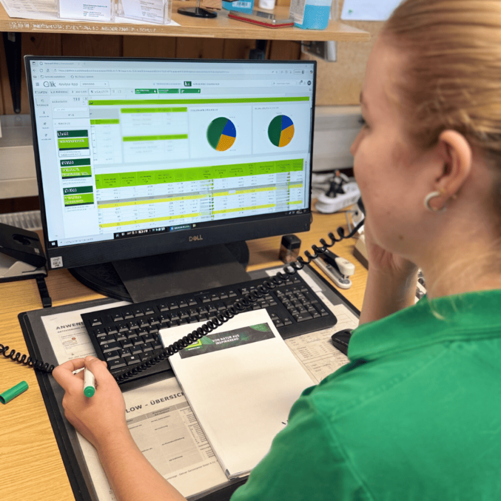 Frau in grünem Shirt sitzt am Schreibtisch und telefoniert