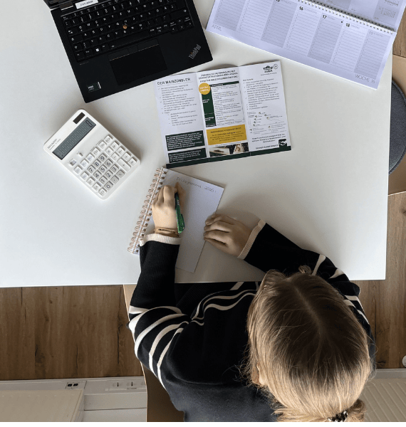 Bild einer Mitarbeiterin am Schreibtisch mit Laptop und Notizbuch