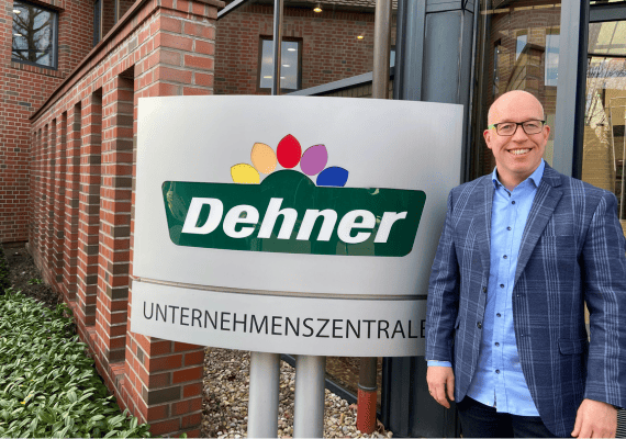 Ein Mann in einem blauen Sakko steht vor einer Firmenzentrale