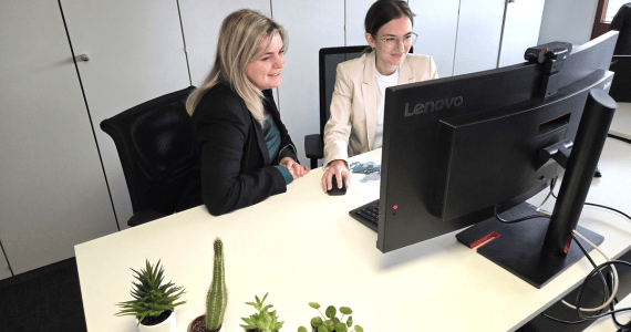 Zwei Frauen im Büro sitzen zusammen an einem Bildschirm