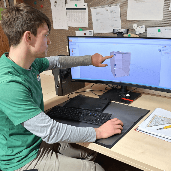 Ein Auszubildender am Schreibtisch zeigt ein Zeichenprogramm auf dem PC-Bildschirm