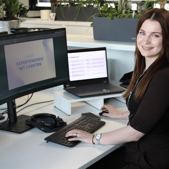 Eine Frau im schwarzen Oberteil sitzt am Schreibtisch und arbeitet am PC