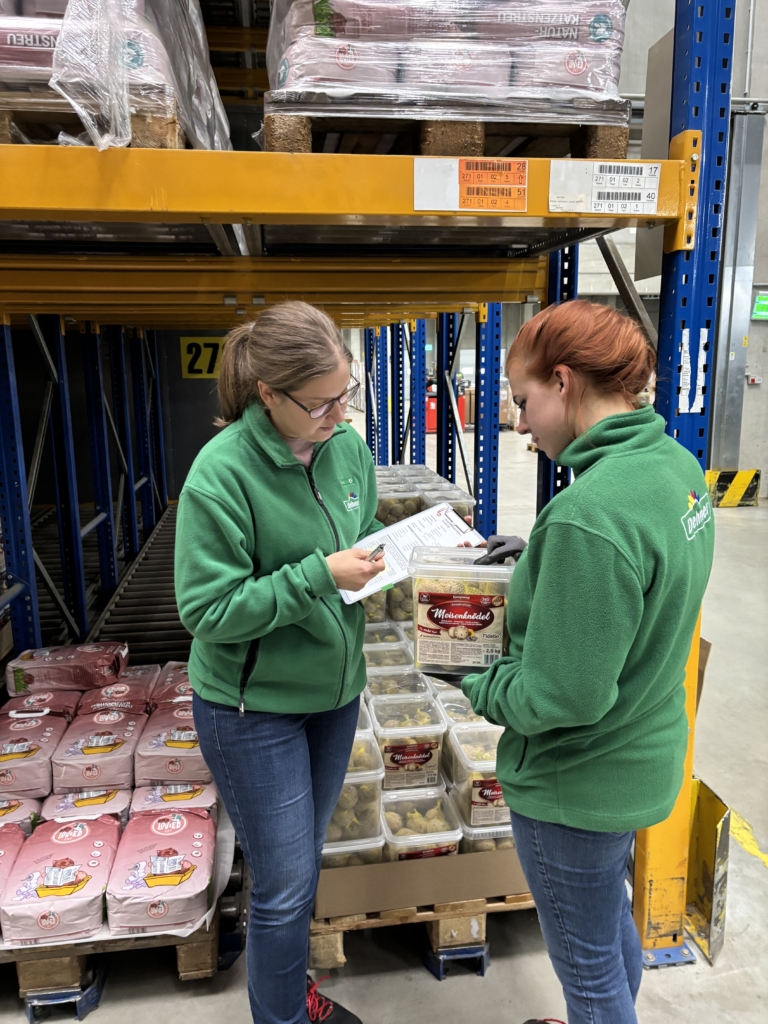 Zwei Frauen stehen in einem Lager und schauen sich ein Dokument an