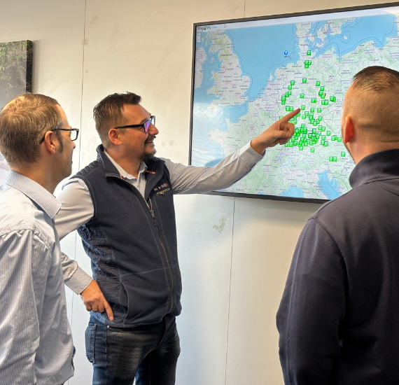 Drei Männer stehen an einem Bildschirm und prüfen eine Landkarte mit grünen Markierungen
