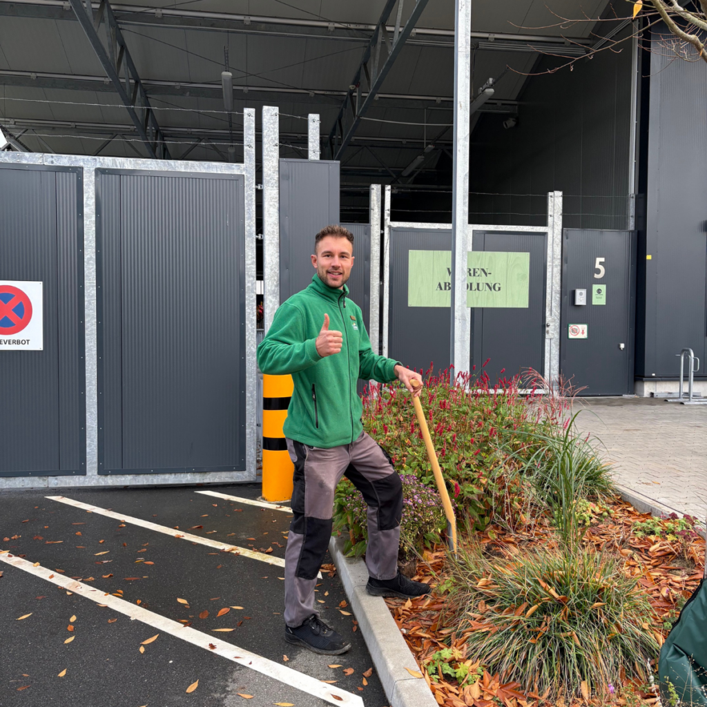 Mann mit grünem Fleece steht mit einem Spaten im Beet