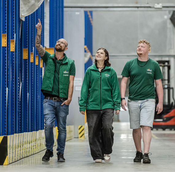 Drei Personen in grünen Oberteilen gehen durch die Logistik