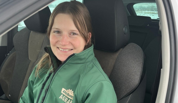 Eine Frau in einer grünen Arbeitsjacke mit Dehner Agrar Logo sitzt in einem Auto