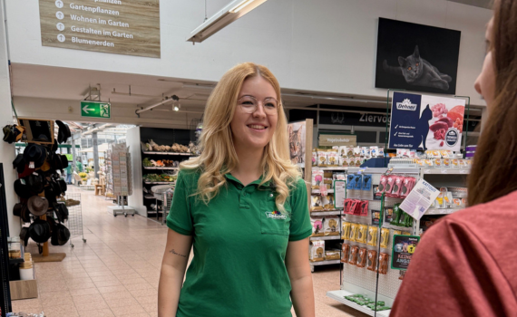 Eine Verkäuferin in einem grünen T-Shirt lächelt freundlich eine Kundin an