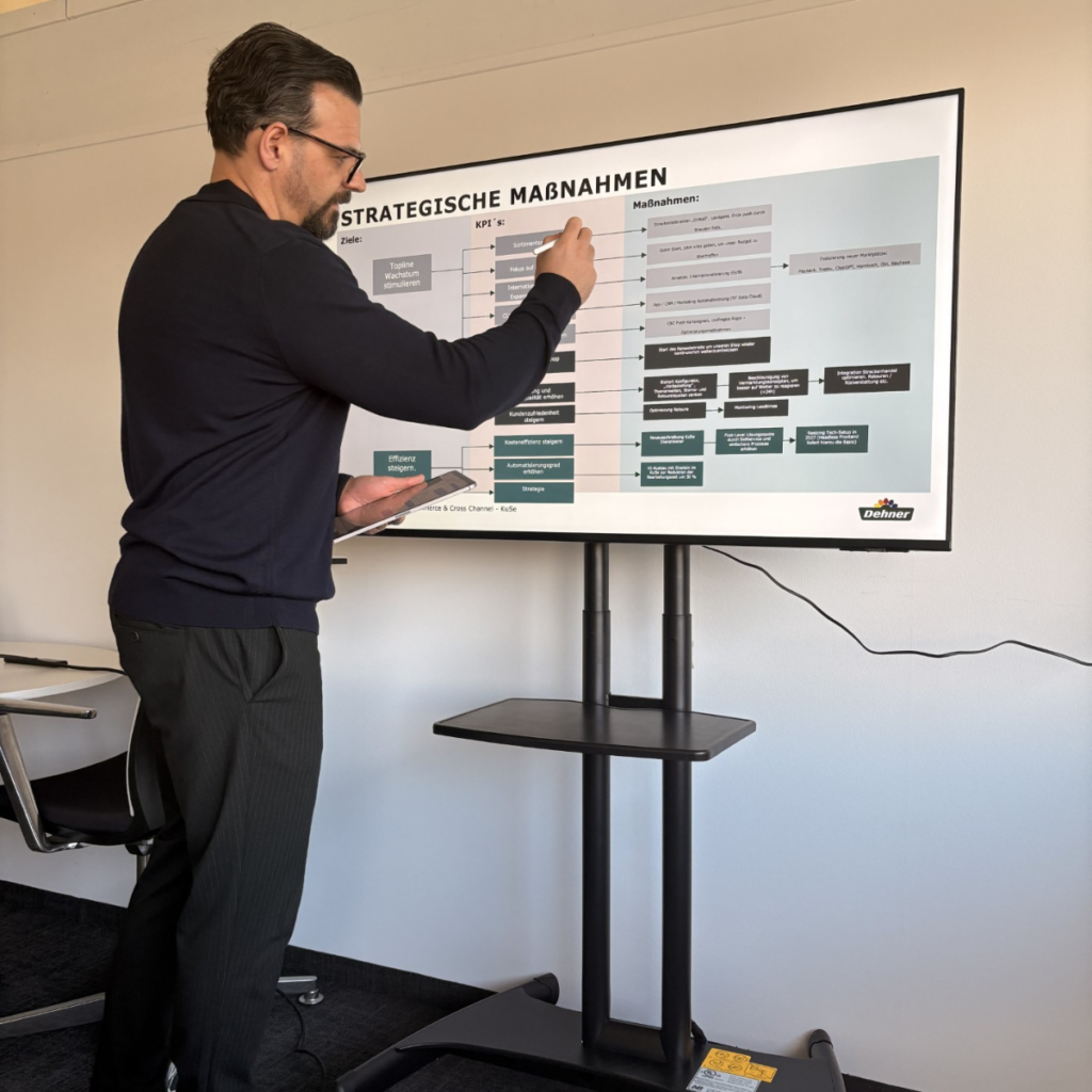 Ein Mann im schwarzen Pullover steht vor einem Bildschirm