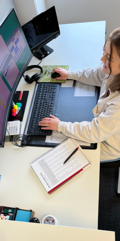 Frau in weißer Bluse sitzt am Schreibtisch und arbeitet am Computer