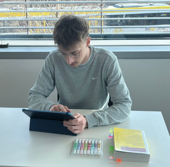 Mann am Laptop mit Gesetzbuch und Textmarker auf dem Tisch