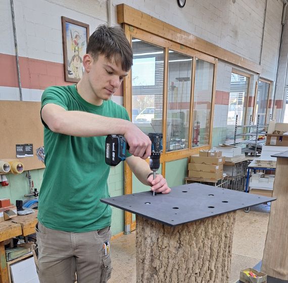 Auszubildender schraubt eine Metallplatte an einen Holzstamm