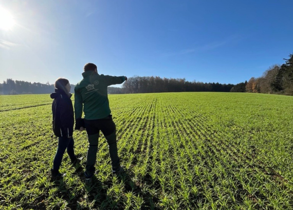 Eine Frau und ein Mann stehen in Dehner Agrar Arbeitskleidung auf einem Feld und begutachten die Getreidepflanzen