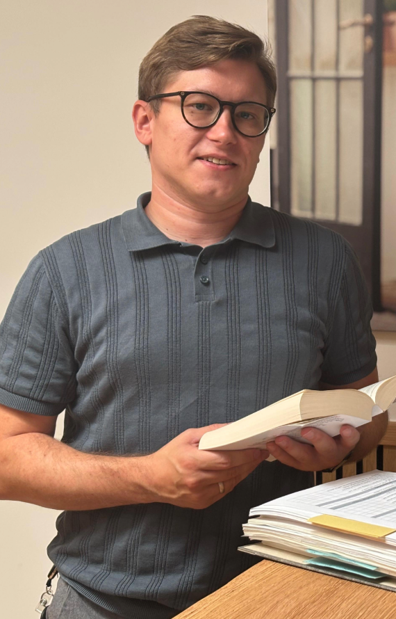Ein Mann in einem grauen T-Shirt hält ein Gesetzbuch in der Hand und lächelt