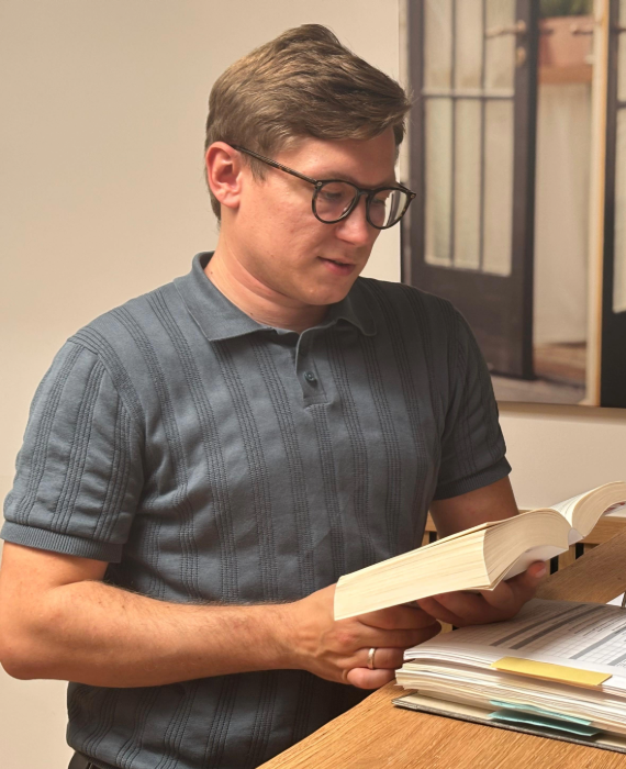 Ein Mann in einem grauen T-Shirt mit Brille liest aufmerksam in einem Gesetzbuch