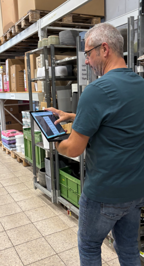 Ein Mann läuft durch ein Lager und wirft einen prüfenden Blick auf seinen Laptop, den er in der Hand hält