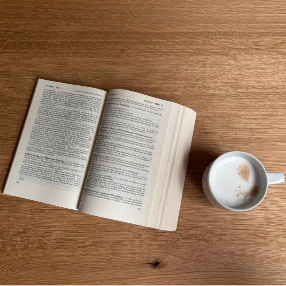 Ein geöffnetes Gesetzbuch liegt, neben einer Tasse Kaffee, auf einem Tisch