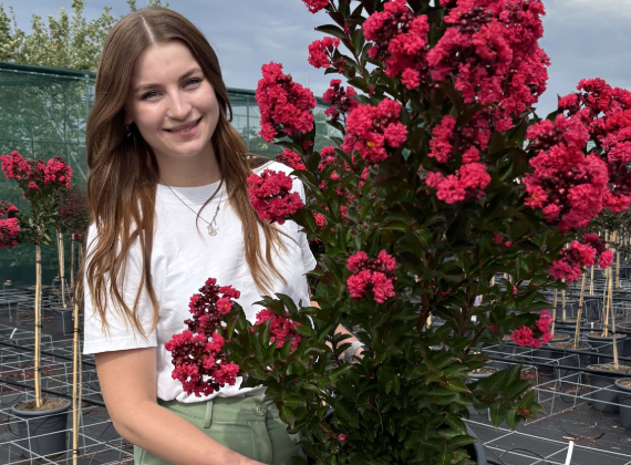Frau hält eine große Pflanze mit pink-roten Blüten in der Hand und lächelt